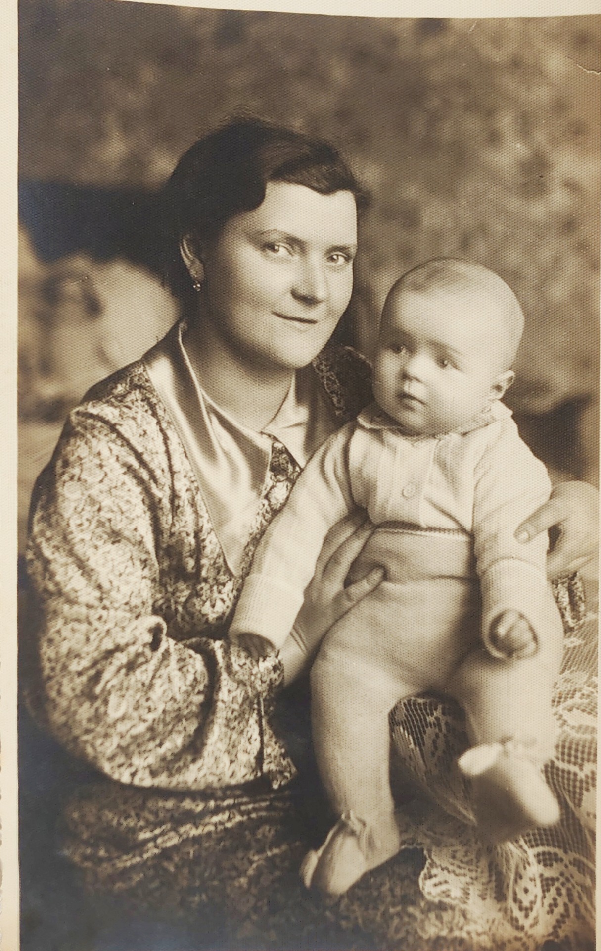 Régi fekete-fehér fotón fiatal nő kisgyerekkel, stúdió háttérrel.