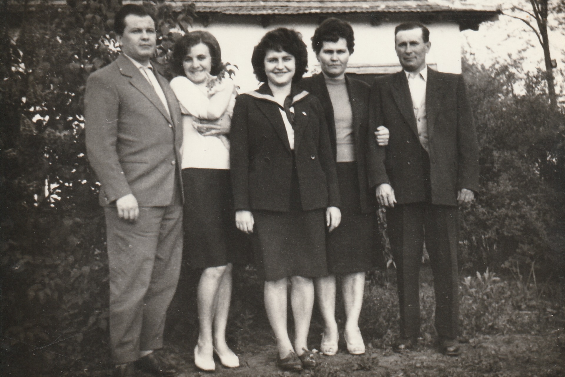 Öt felnőtt áll családi fotón, kertben, régi fekete-fehér öltönyökben és ruhákban.